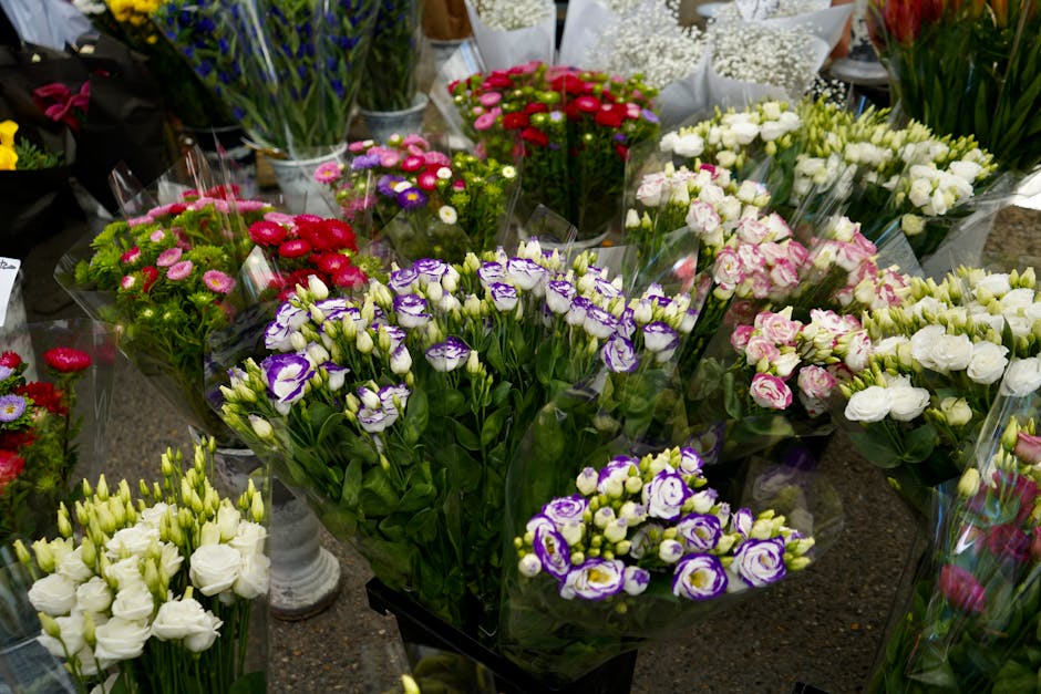 An assortment of fresh flower bouquets displayed on a table at a florist shop, featuring various flower types including pink, red, white, purple, and violet blooms. The arrangements are wrapped in cle